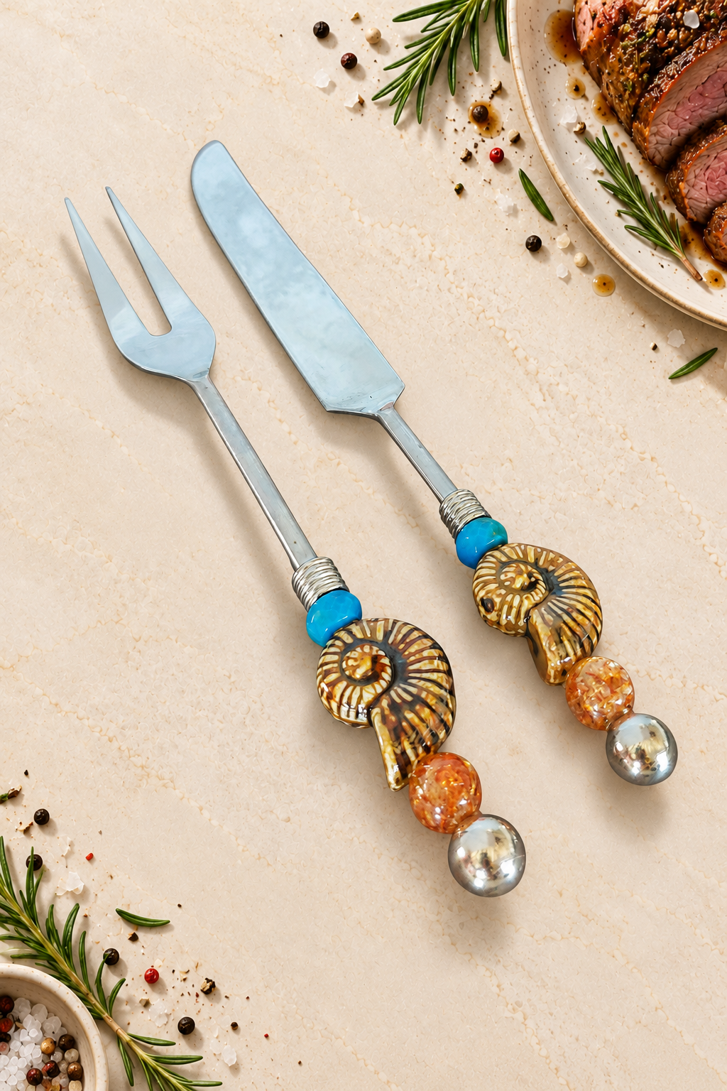 The Afiyah decorative carving set with a silver-coloured carving knife and two-pronged fork, featuring blue beads, spiral ammonite details, amber-coloured glass beads and polished silver end beads.