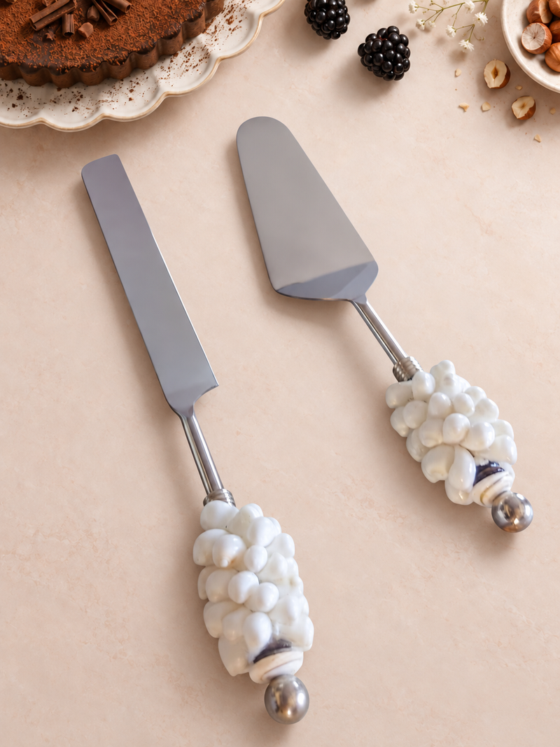 The Athira decorative cake serving set with a silver-coloured cake knife and cake server, textured white shell-style handles and polished silver end beads.