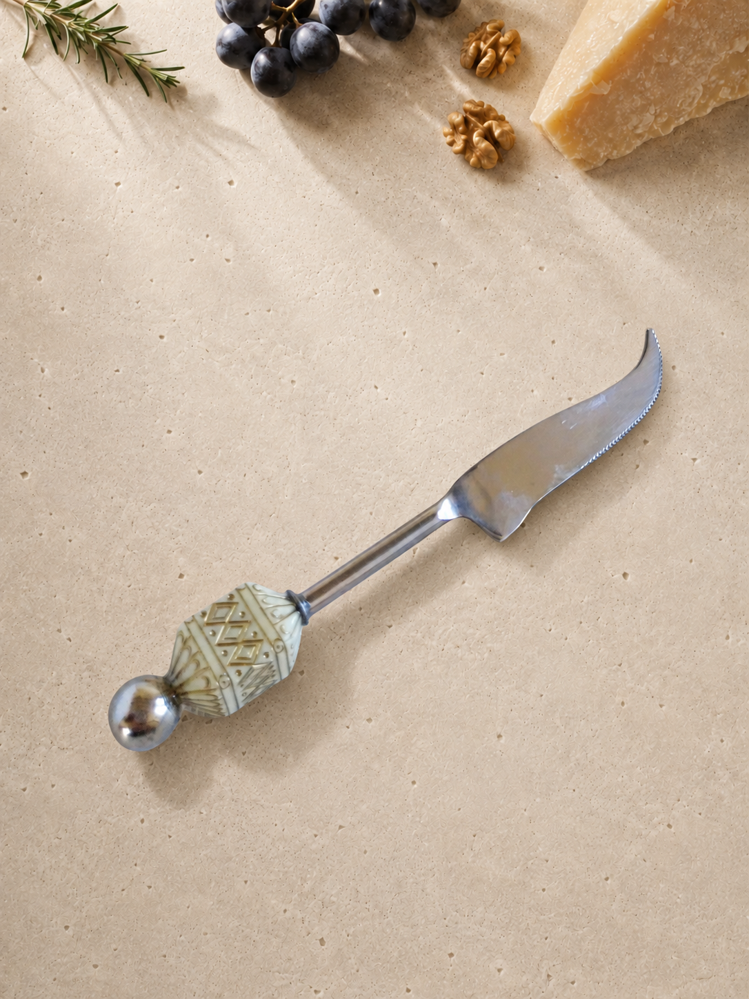 The Badee decorative cheese knife with a silver-coloured curved blade, an ivory patterned bead and a polished silver end bead.