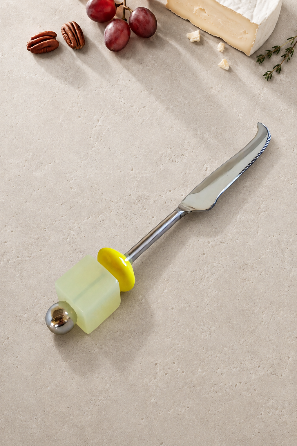 The Emrah cheese knife featuring a silver-coloured curved blade, a translucent pale yellow bead, a bright yellow disc bead and a polished silver end bead.