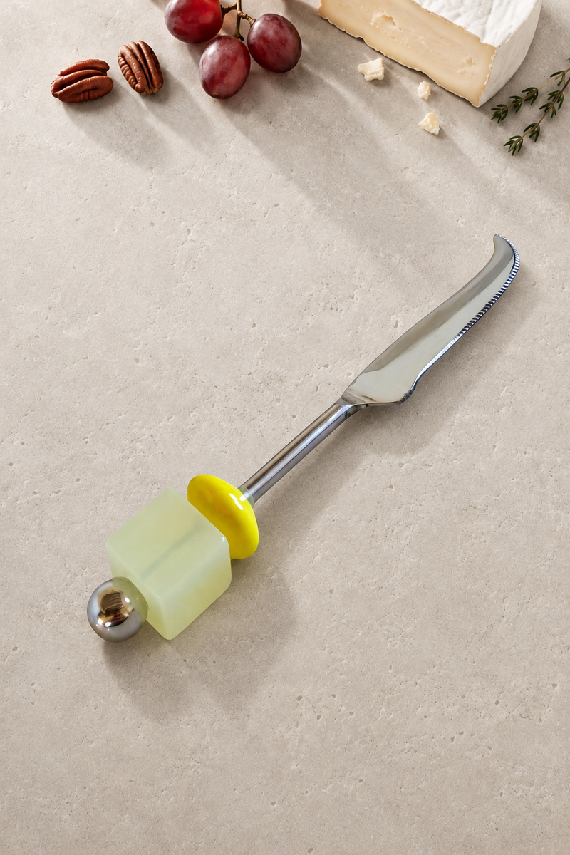 The Emrah cheese knife featuring a silver-coloured curved blade, a translucent pale yellow bead, a bright yellow disc bead and a polished silver end bead.