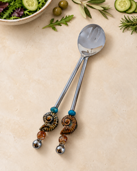 The Hanai decorative salad serving set with a silver-coloured spoon and slotted server, blue accent beads, spiral ammonite details and amber-coloured glass beads.