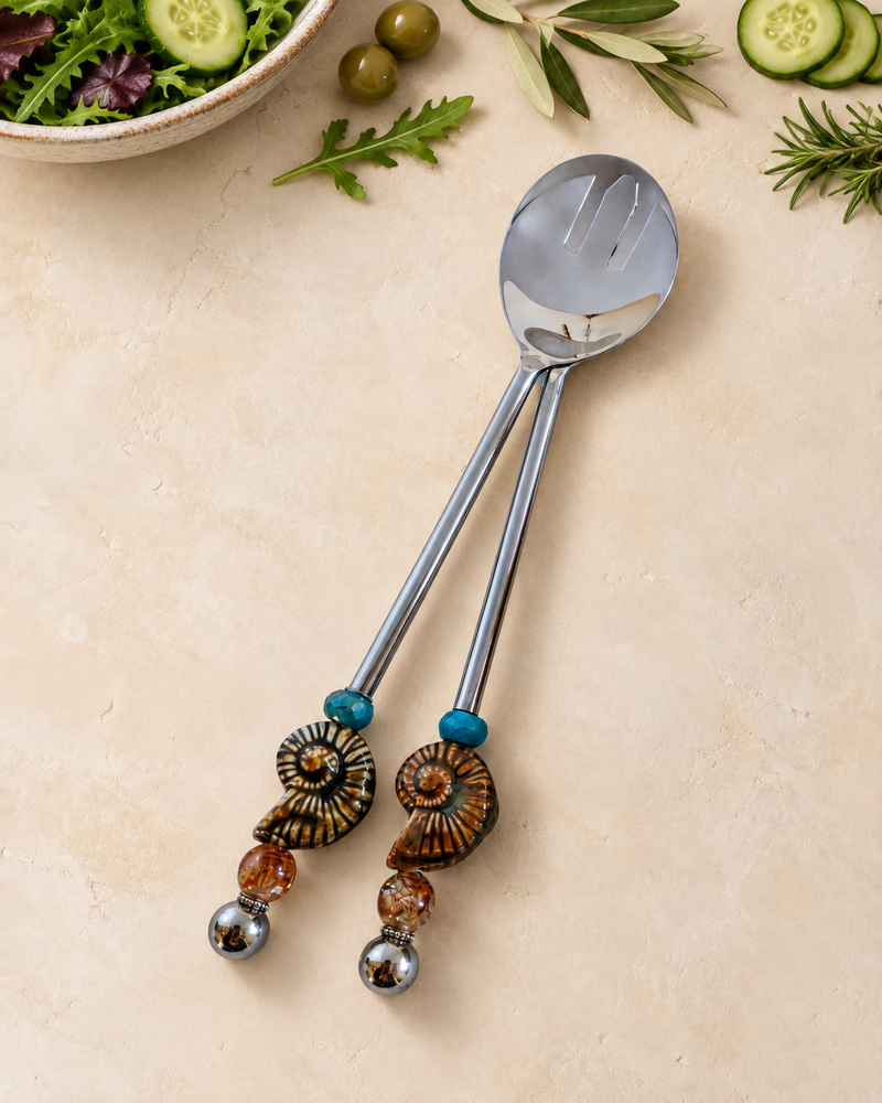 The Hanai decorative salad serving set with a silver-coloured spoon and slotted server, blue accent beads, spiral ammonite details and amber-coloured glass beads.