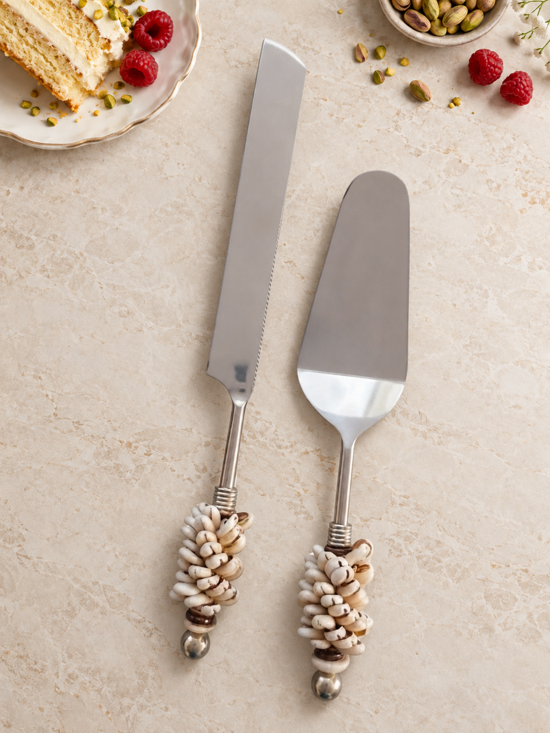 The Hibah cake serving set featuring a silver-coloured cake knife and cake server with decorative Cowri shell handles, natural brown accents and polished silver end beads.