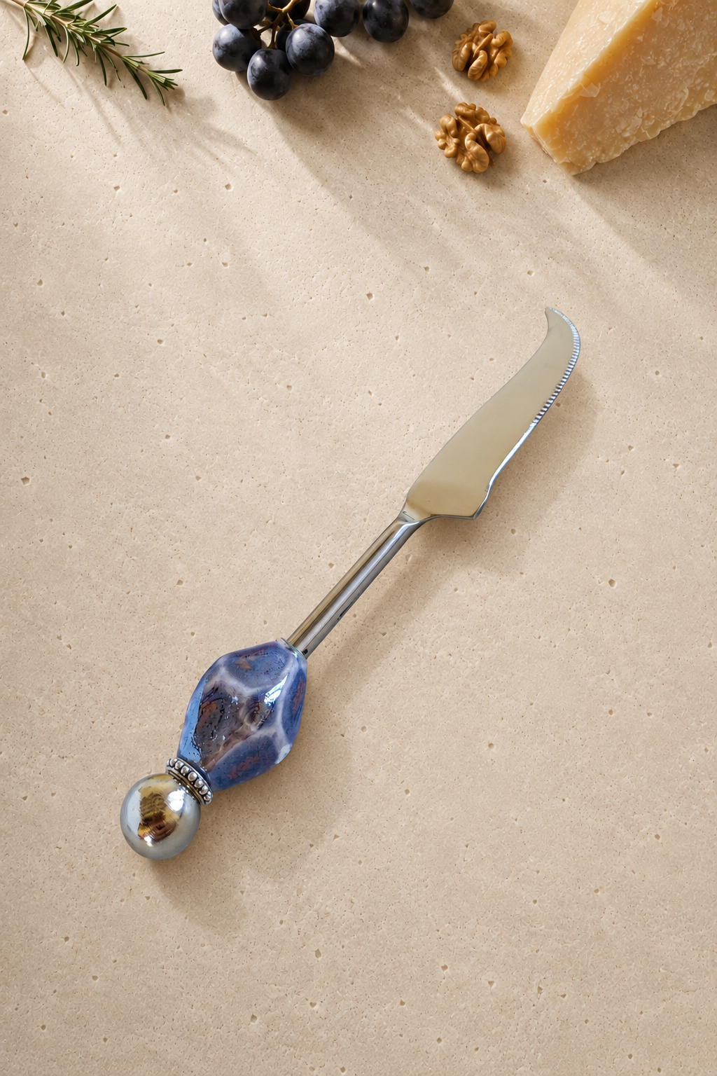 The Kabir decorative cheese knife with a silver-coloured curved blade, a faceted blue and purple marbled bead and a polished silver end bead.