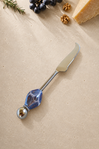 The Kabir decorative cheese knife with a silver-coloured curved blade, a faceted blue and purple marbled bead and a polished silver end bead.