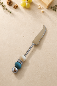 The Kasra cheese knife featuring a silver-coloured curved blade, an ivory bead, a matte blue accent bead and a polished silver end bead.