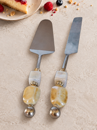 The Malina decorative cake serving set with a silver-coloured cake knife and cake server, cream and honey-coloured marbled beads, square pearlescent accents and polished silver end beads.