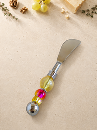 The Mansur decorative cheese knife with a silver-coloured curved blade, translucent yellow glass bead, bright pink accent bead, yellow faceted bead and polished silver end bead.