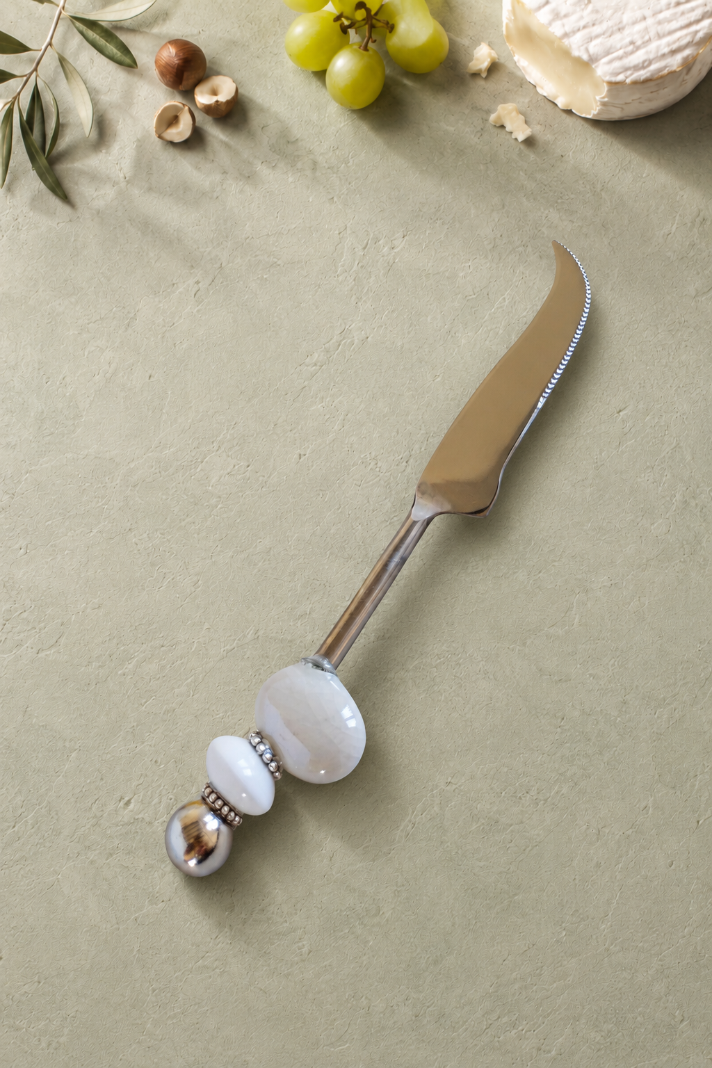 The Masoom decorative cheese knife with a silver-coloured curved blade, a large pearlescent white bead, a smaller white accent bead and a polished silver end bead.