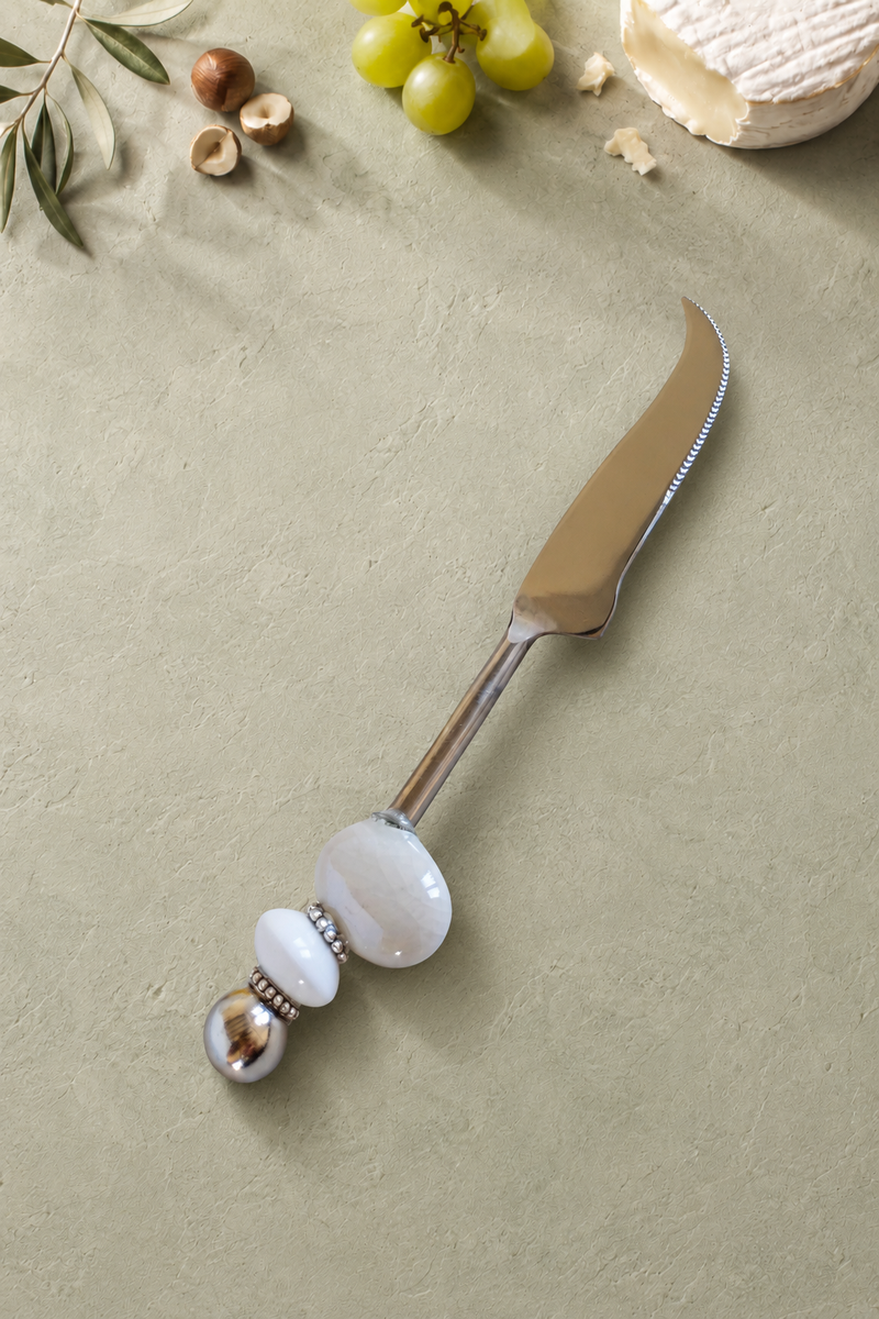 The Masoom decorative cheese knife with a silver-coloured curved blade, a large pearlescent white bead, a smaller white accent bead and a polished silver end bead.