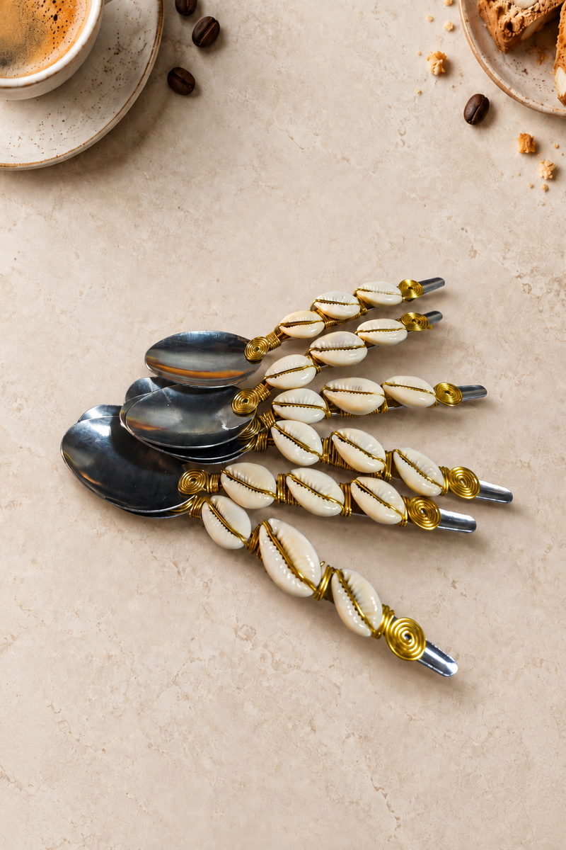 The Myra set of 6 coffee spoons featuring silver-coloured spoon heads, white cowrie shells with gold-coloured accents, decorative gold wire wrapping and spiral details.