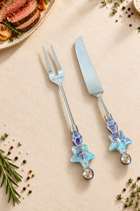 The Yuhan decorative carving set with a silver-coloured carving knife and two-pronged fork, featuring blue and purple glass beads, turquoise starfish details and polished silver end beads.