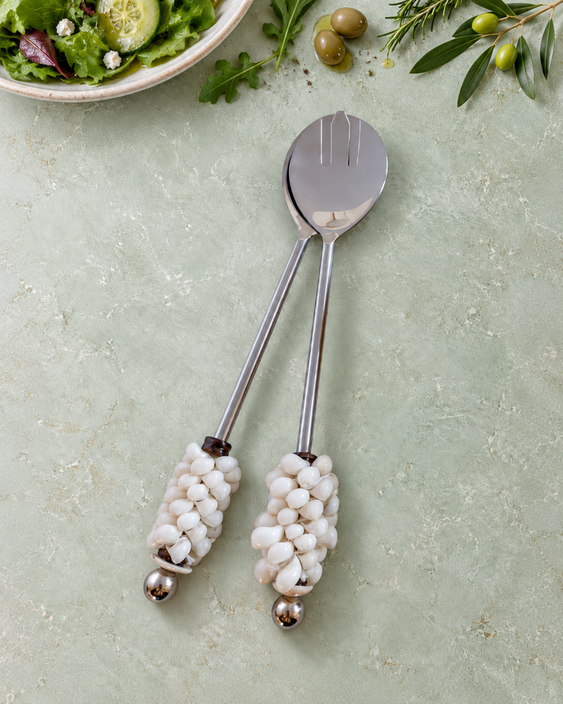 The Devina salad serving set featuring a silver-coloured spoon and slotted server with square pearlescent beads, ivory spiral shell details and polished silver end beads.