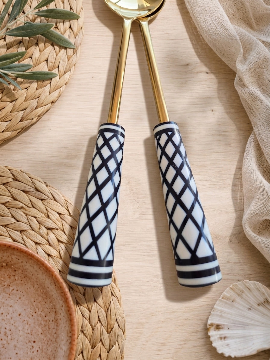 Close up of the Savira gold salad servers with black and white patterned handles